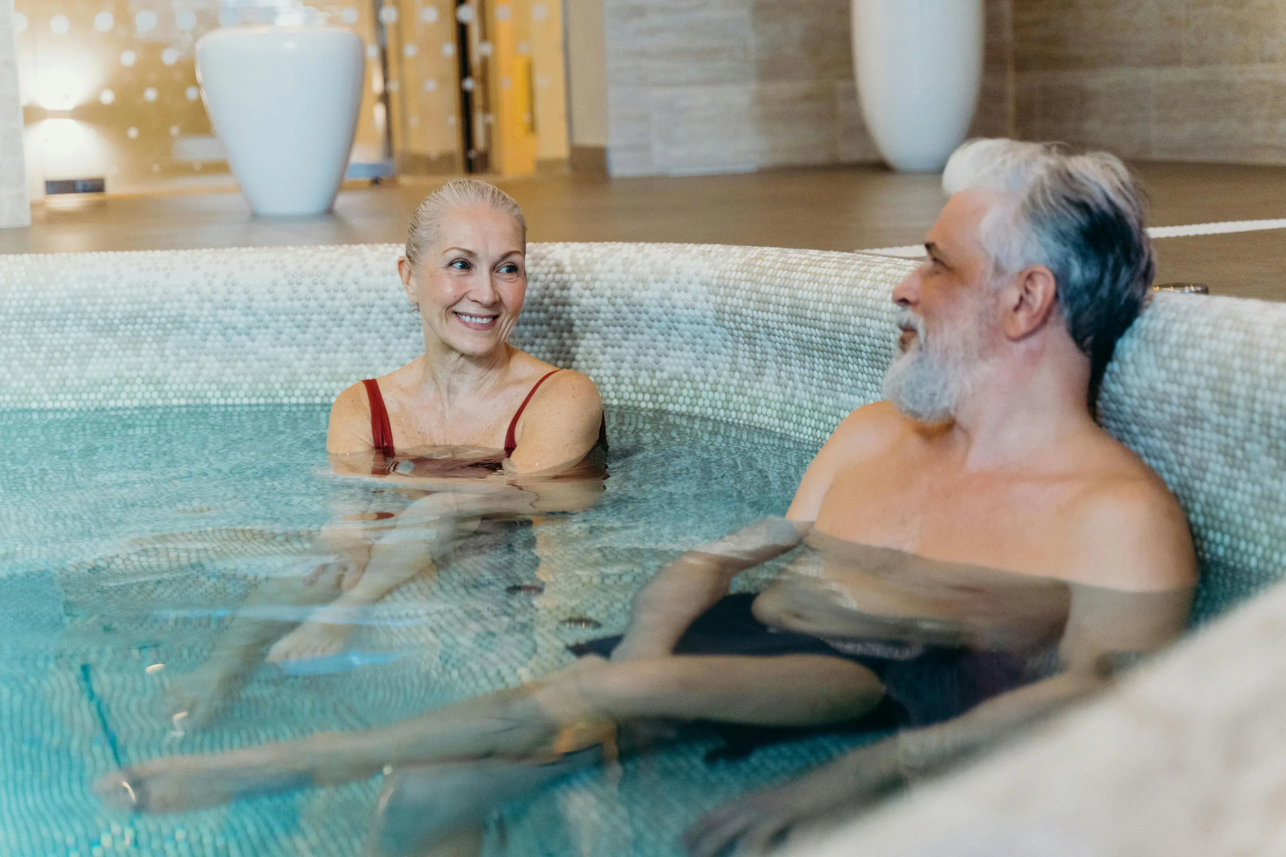 Two seniors grin at each other while soaking in a hot tub