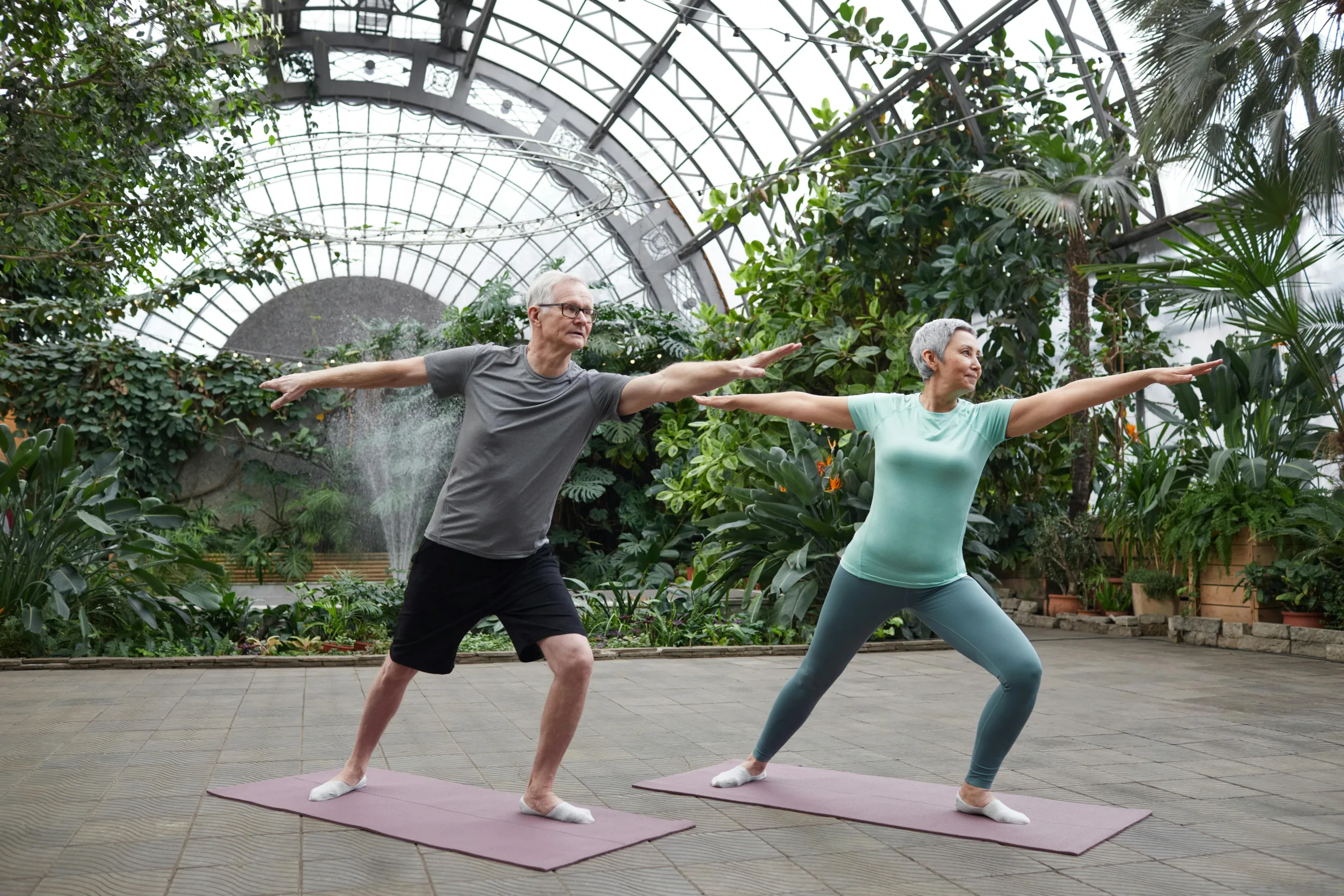 Two serene looking seniors practice yoga in an indoor garden