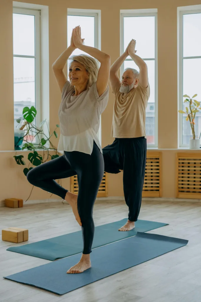 Two seniors do yoga in a spacious room