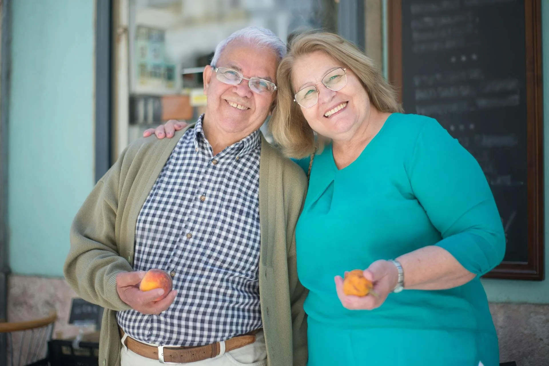 An elderly couple hugs and smiles while holding peaches