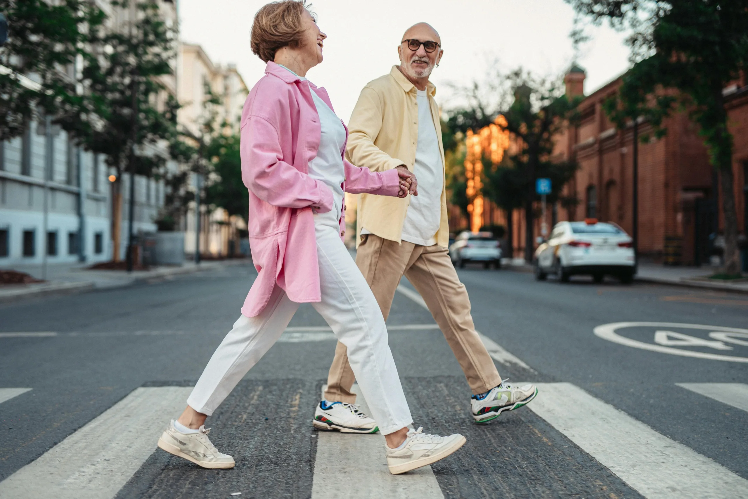 Two laughing seniors hold hands as they cross the street