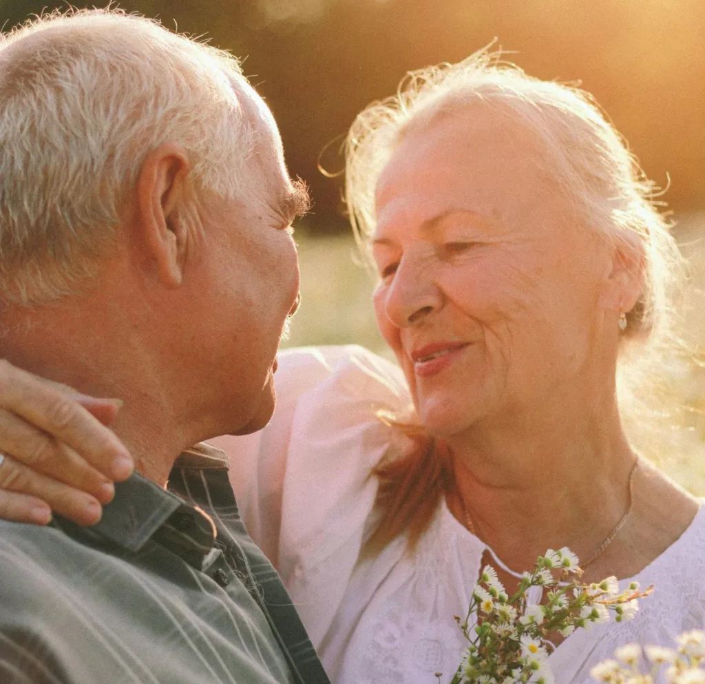 Two seniors in a field smile at each other and hug