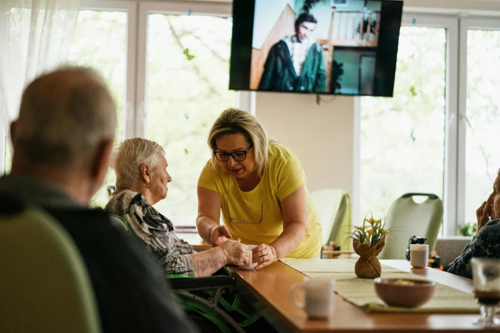 A woman with glasses helps an elderly lady with her drink