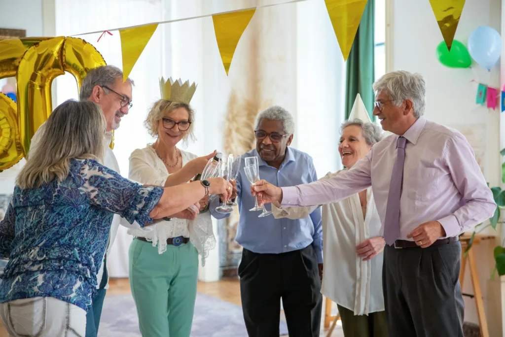 A group of smiling seniors wearing party hats toast their champagne glasses