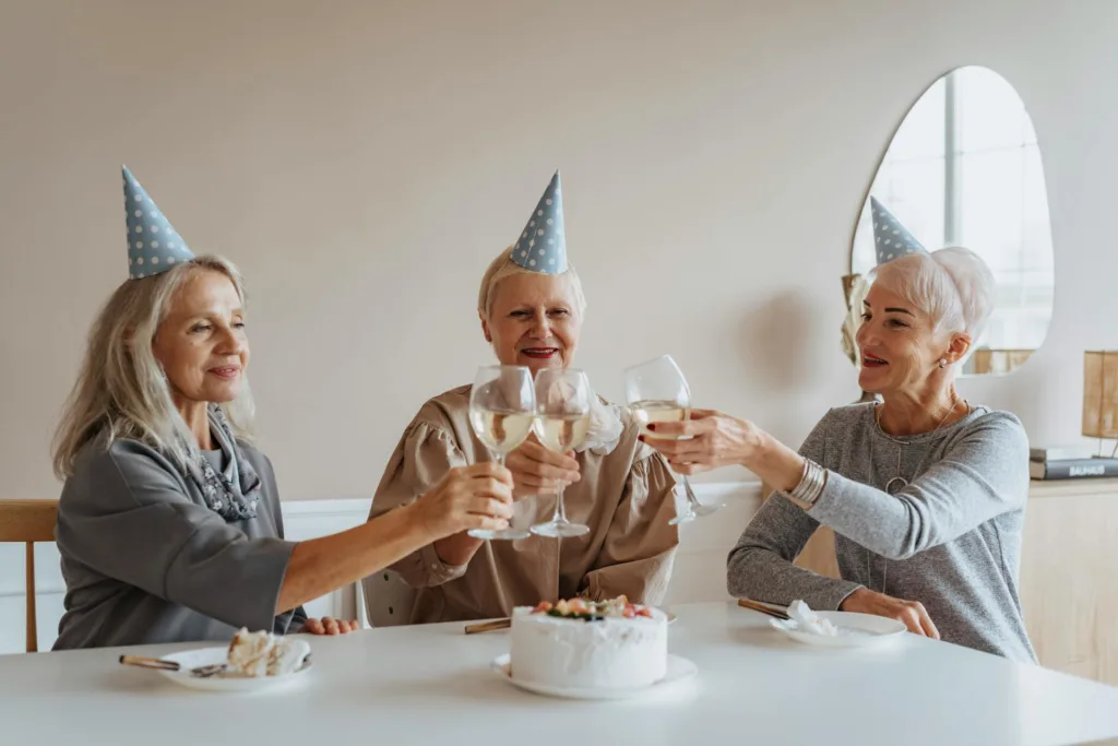 Three senior woman sit at a table with cake and toast their glasses