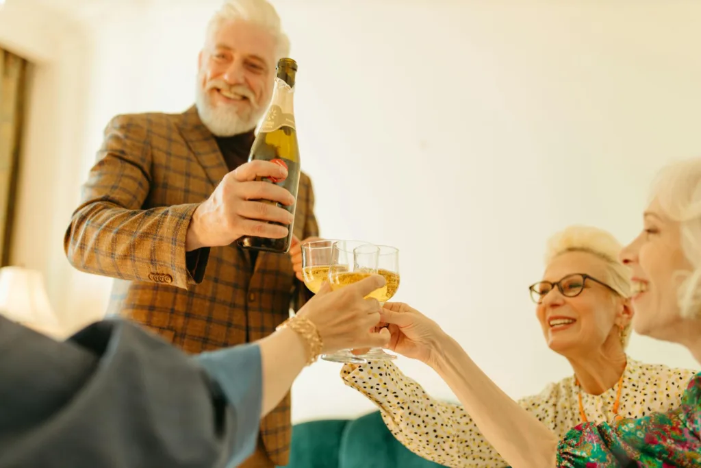 A group of seniors with wine glasses toast while a smiling elderly man holds a drink bottle